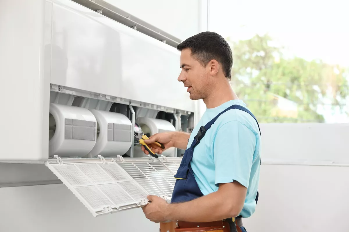 Professional HVAC technician in a tool belt inspecting an air conditioner filter during a routine maintenance check in Durham.