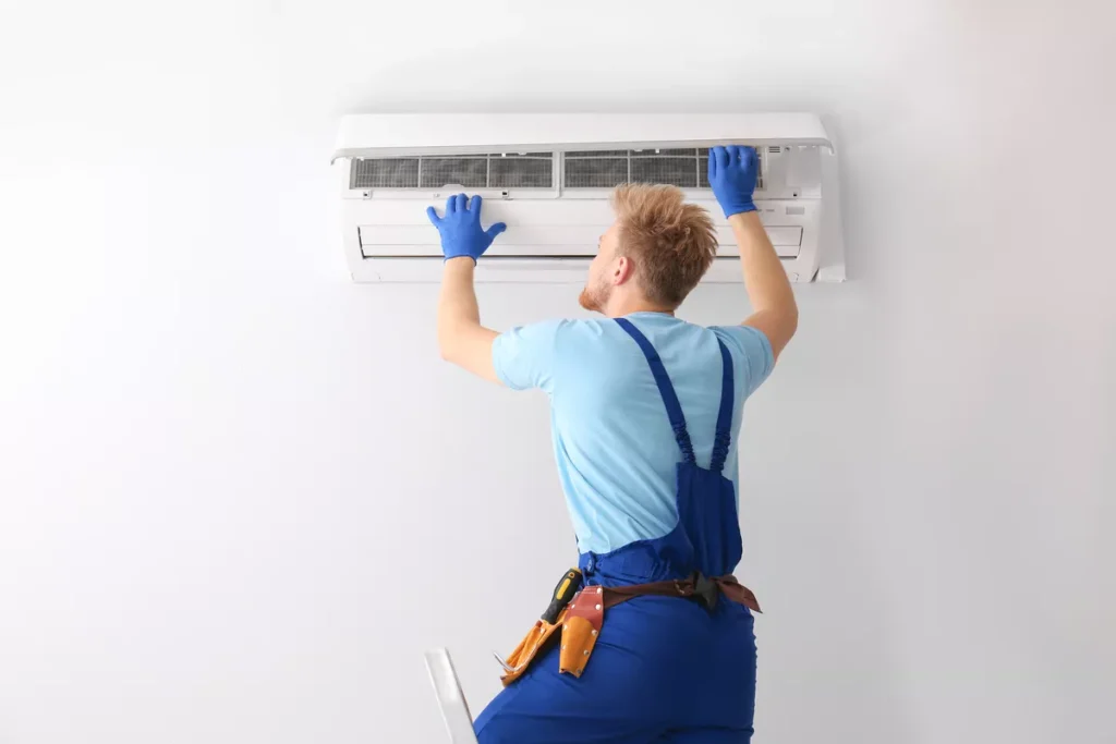 Professional HVAC technician on a ladder inspecting a wall-mounted AC unit in a bright Durham, NC interior.