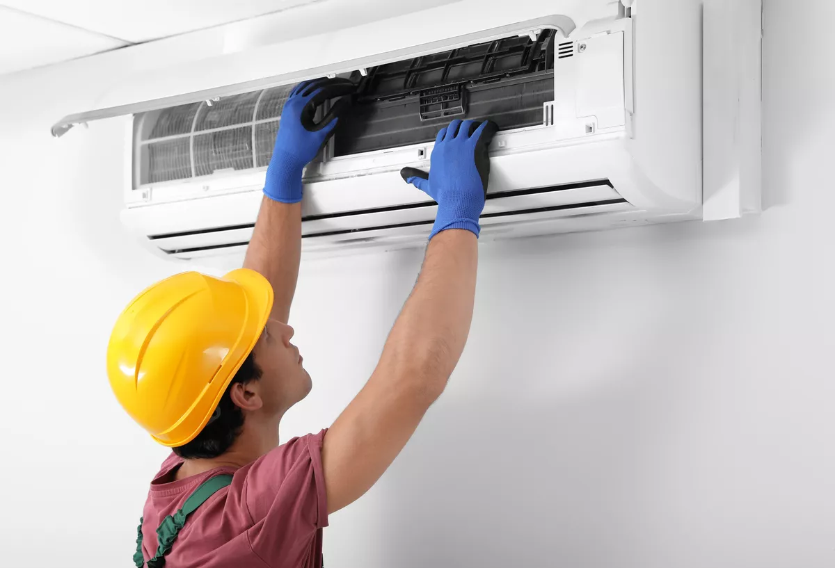 Safety-certified technician wearing a hardhat and protective gloves servicing a wall-mounted air conditioner in Durham.