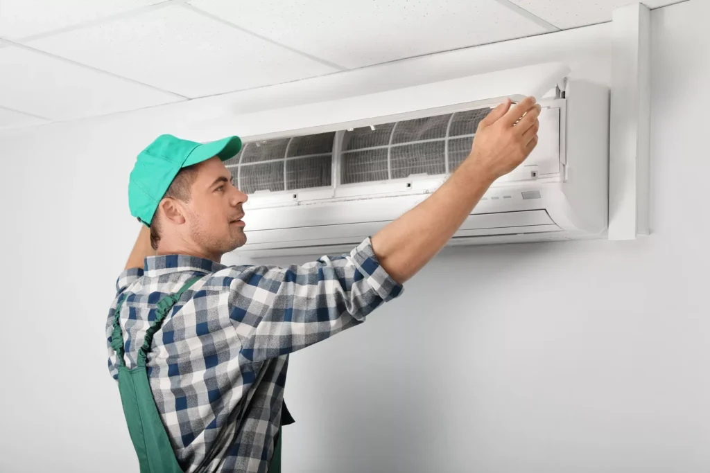 A professional HVAC specialist in a green cap and overalls performing routine maintenance on a residential AC unit in Durham, North Carolina.
