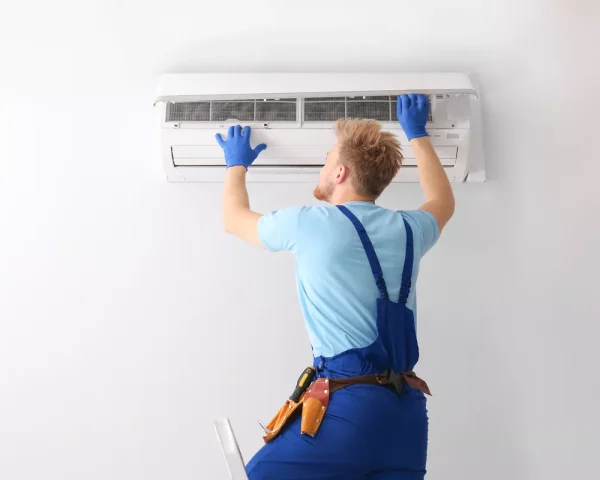 Professional HVAC technician on a ladder inspecting a wall-mounted AC unit in a bright Durham, NC interior.