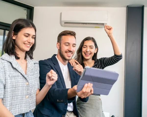 A diverse team of young HVAC professionals in a bright Durham office celebrating a successful project completion on a digital tablet.